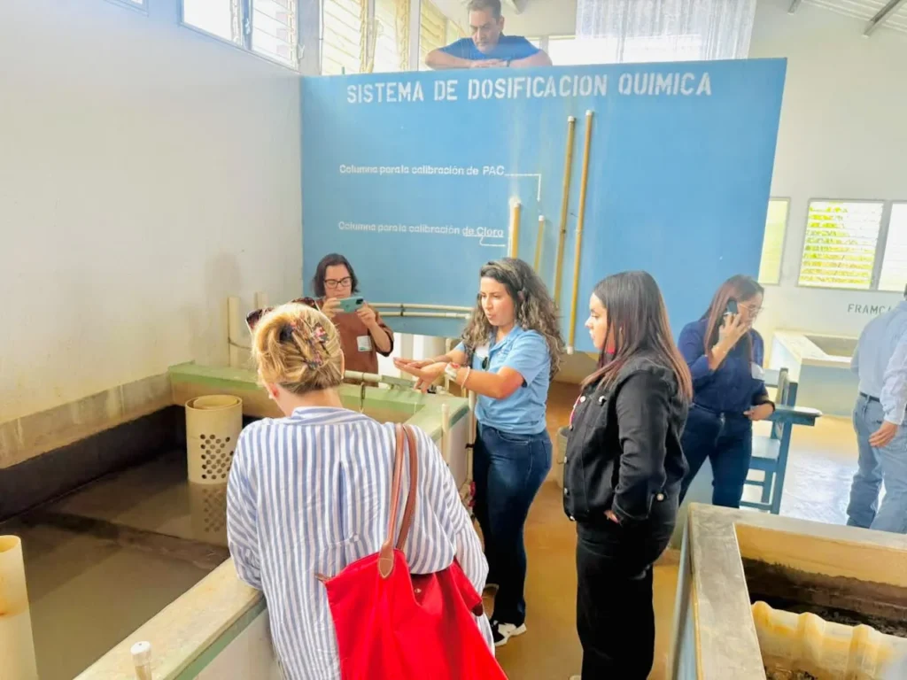 Una integrante del equipo explica el sistema de dosificación química de una planta AguaClara a los participantes
