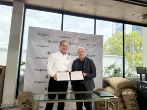 Representantes de Espresso Americano y Universidad Zamorano muestran el convenio firmado frente a un banner de ambas instituciones